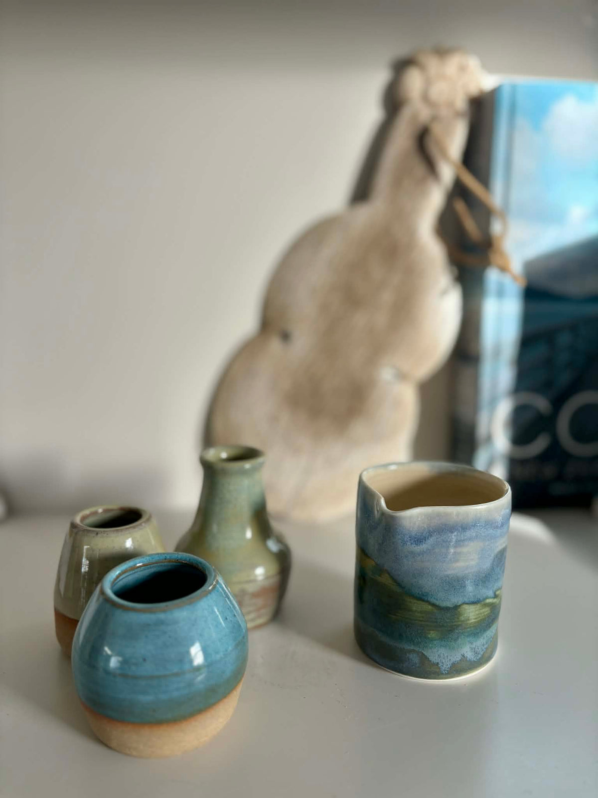 Coastal landscape ceramic jug styled with bud vases and ceramic pieces on a white shelf