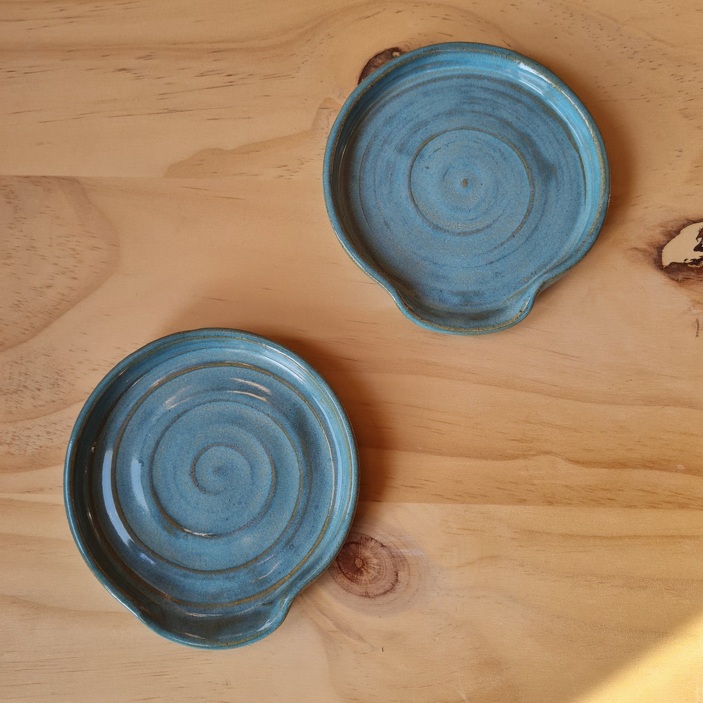 Two rustic blue spoon rests on a plywood background