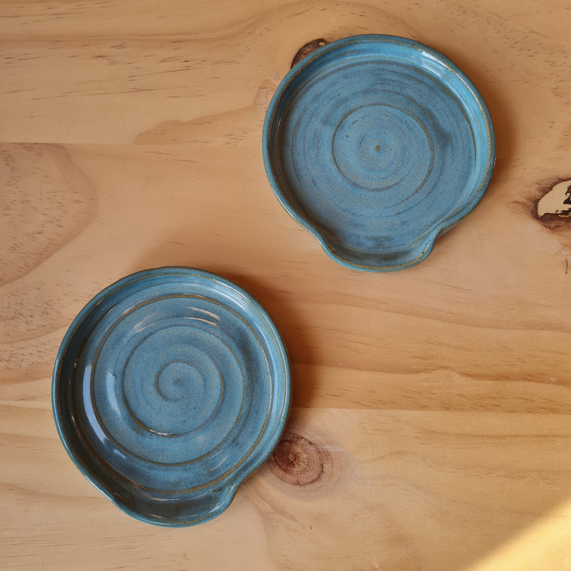 Two rustic blue spoon rests on a plywood background