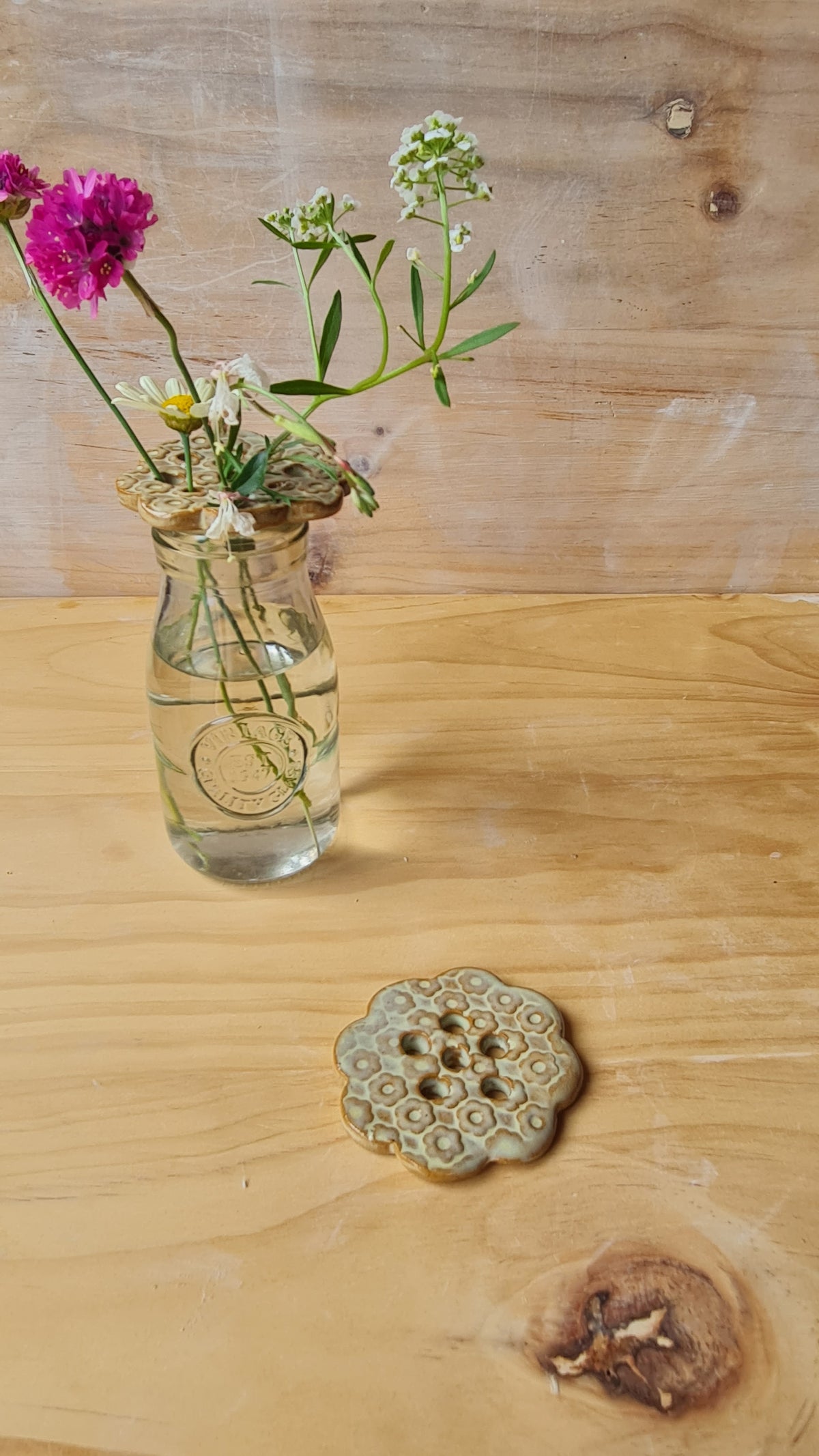 Seagrass green ceramic flower frog holding wildflowers in a glass jar, with a second frog flat showing honeycomb texture detail, on a wooden surface 