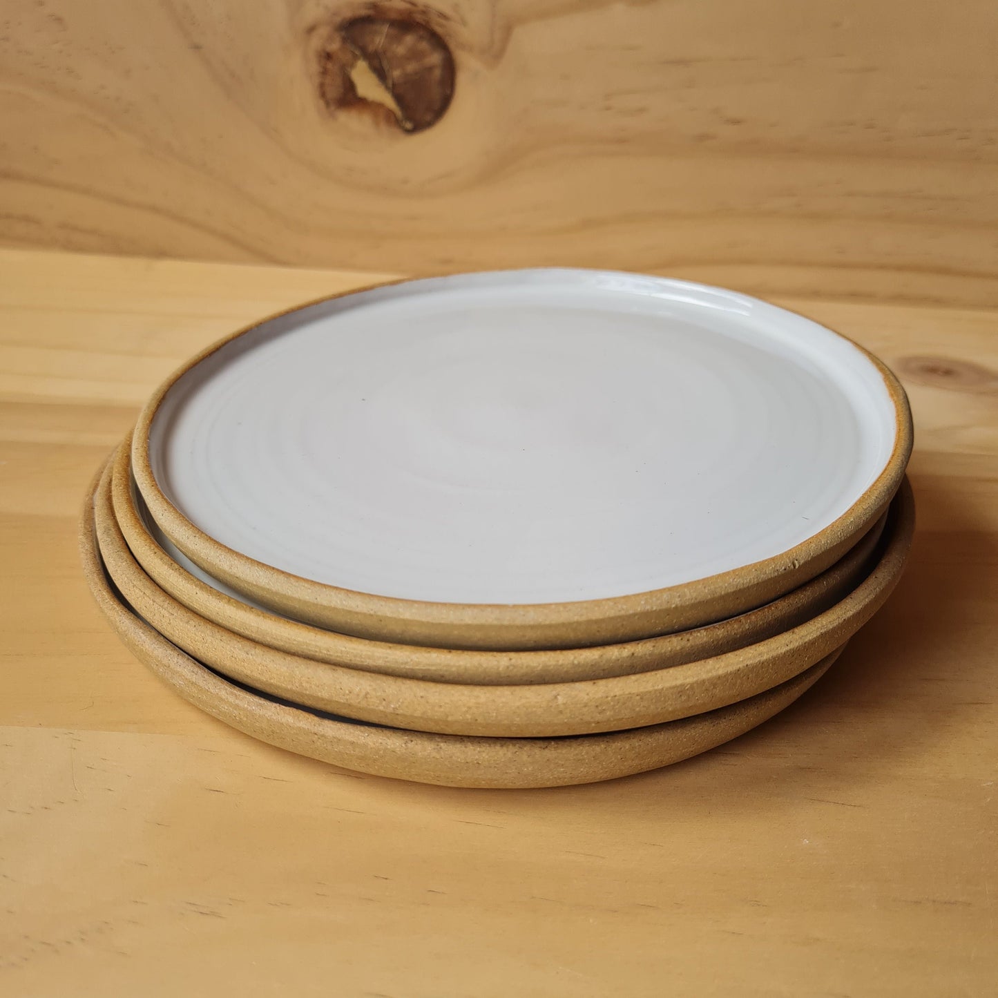 Four white ceramic plates with buff edge stacked on plywood background