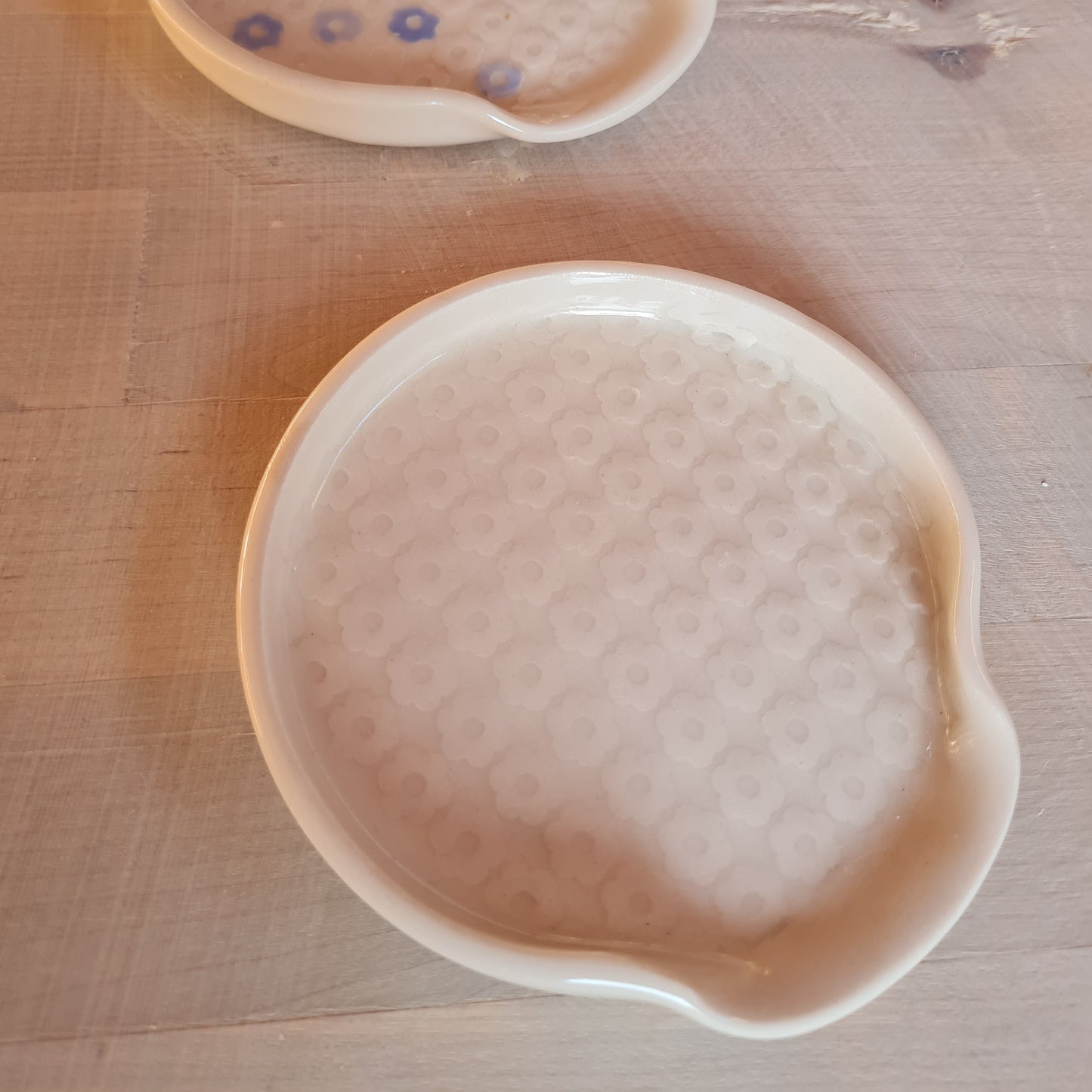 White ceramic spoon rest, with small flowers imprinted into clay.  