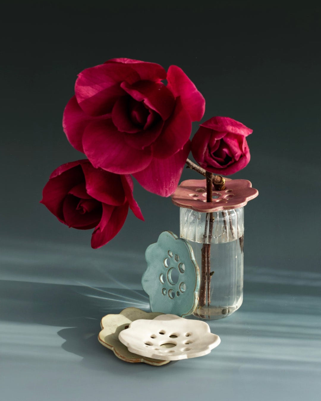Ceramic flower frog in pink holding red roses in a glass jar, with rustic blue, white and seagrass green frogs alongside.