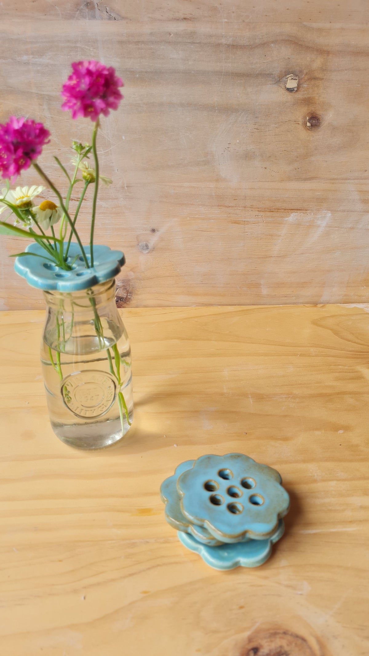 Rustic blue ceramic flower frog holding wildflowers in a glass jar, with two stacked rustic blue frogs on a wooden surface 