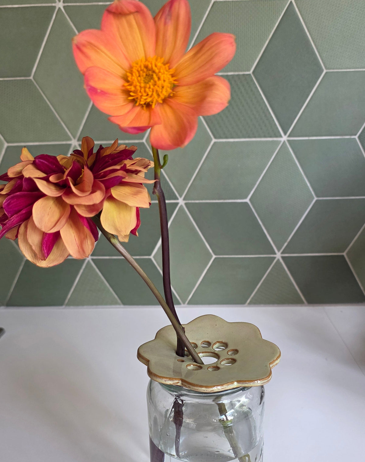 Seagrass green ceramic flower frog holding dahlias in a glass jar, green tile backdrop