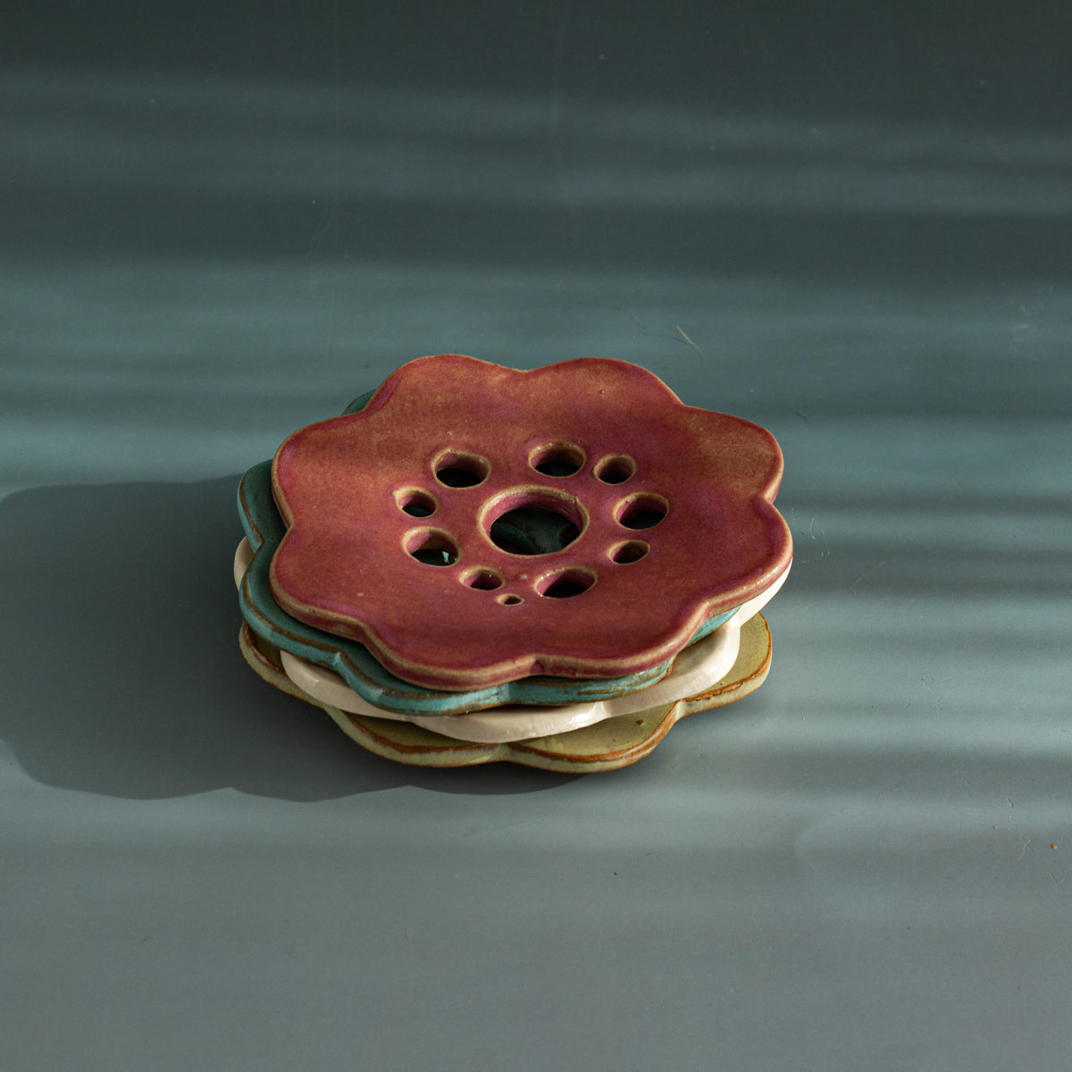 Stack of four handmade ceramic flower frogs in pink, rustic blue, white and seagrass green glazes 