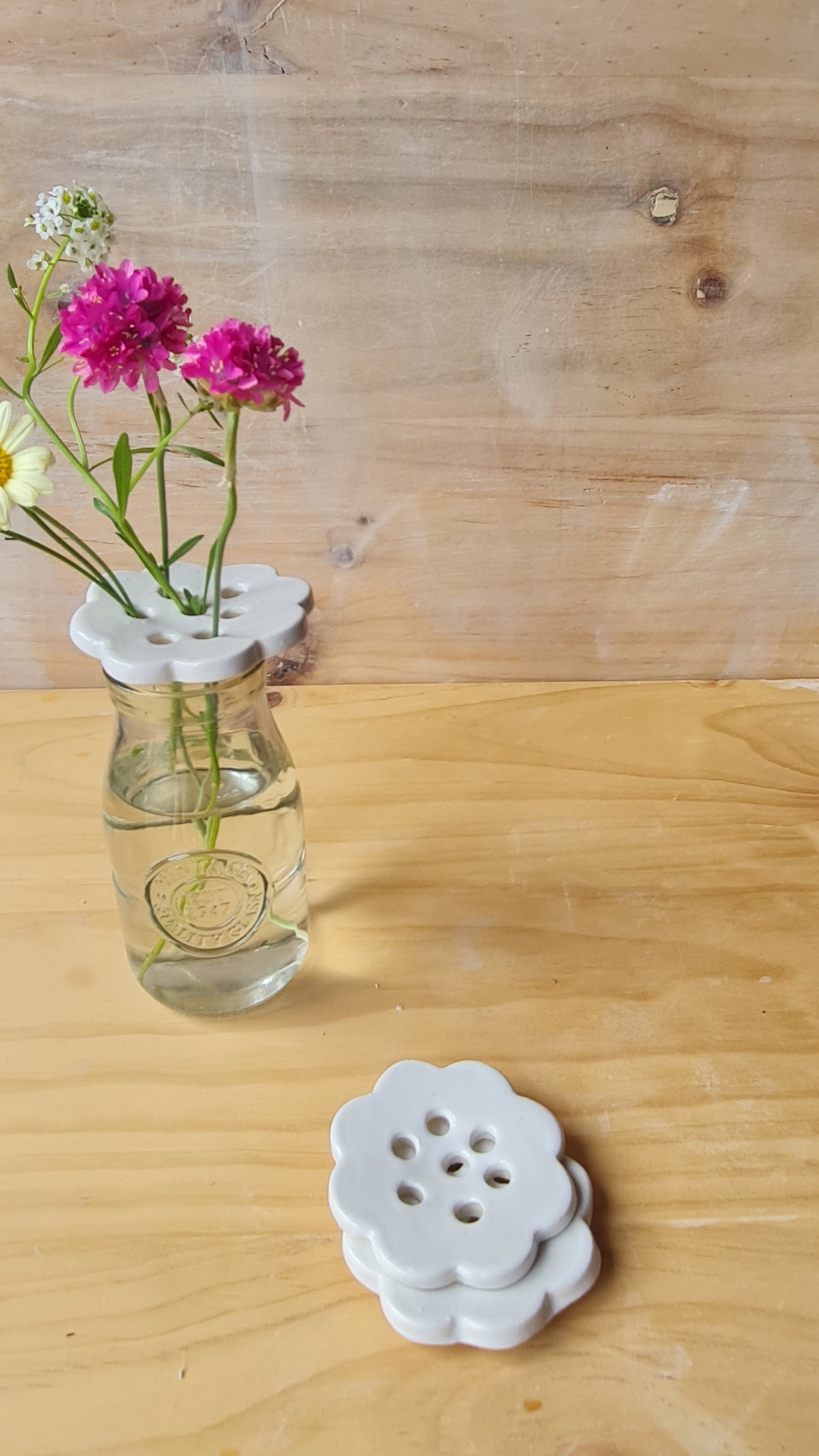 White ceramic flower frog holding wildflowers in a glass jar, with two stacked white frogs on a wooden surface 