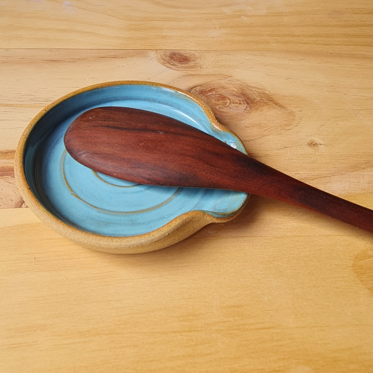 Rustic blue ceramic spoon rest with wooden spoon resting in it, on a wooden surface 