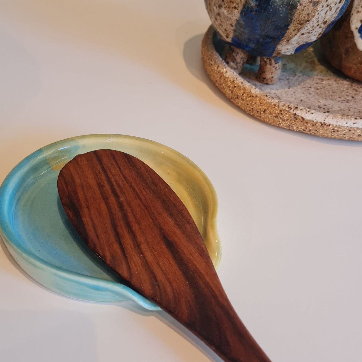 Seagrass green ceramic spoon rest with wooden spoon, styled with coastal ceramic pieces on a white surface 