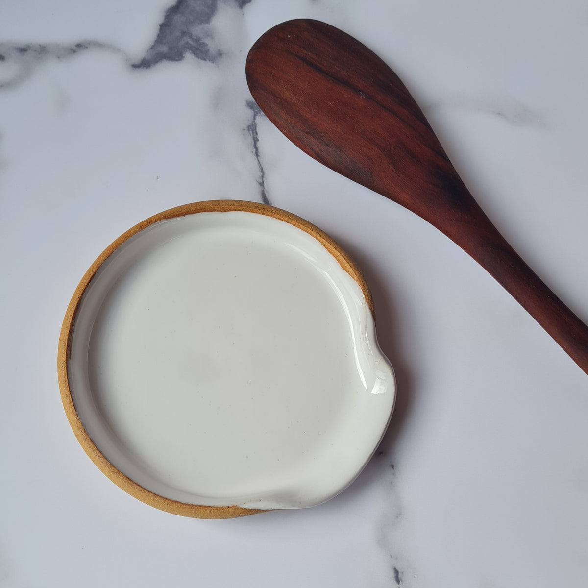 Overhead view of white ceramic spoon rest with wooden spoon on a marble surface