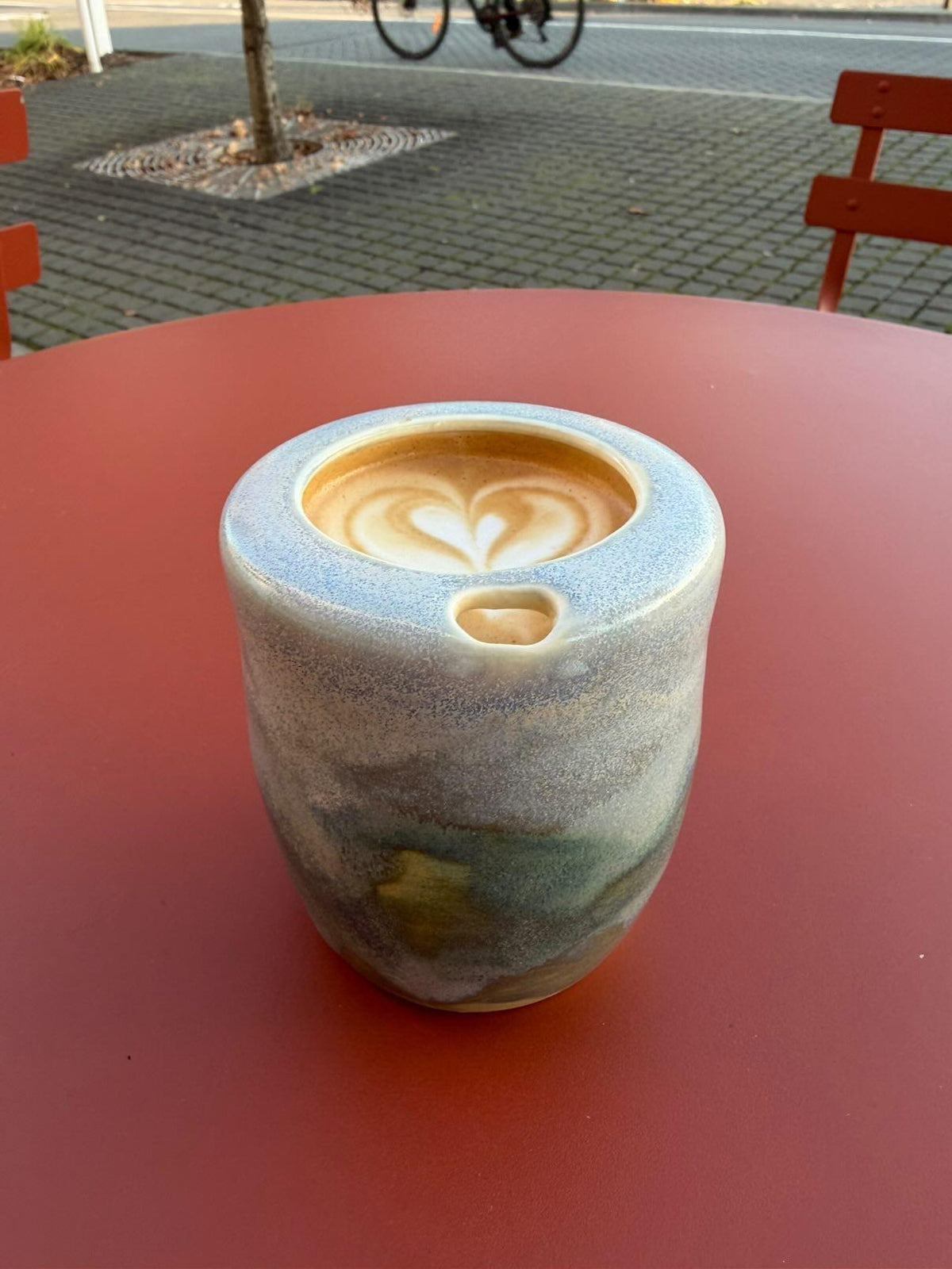 Coastal glaze ceramic takeaway tumbler with latte art on a red outdoor cafe table 