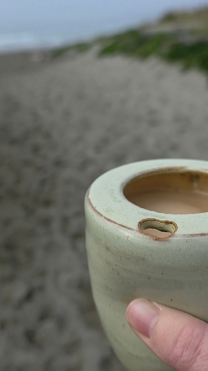Seagrass green ceramic takeaway tumbler held at the beach with coffee inside 