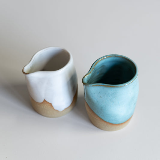two small jusgs on a white bench, one white one blue glaze